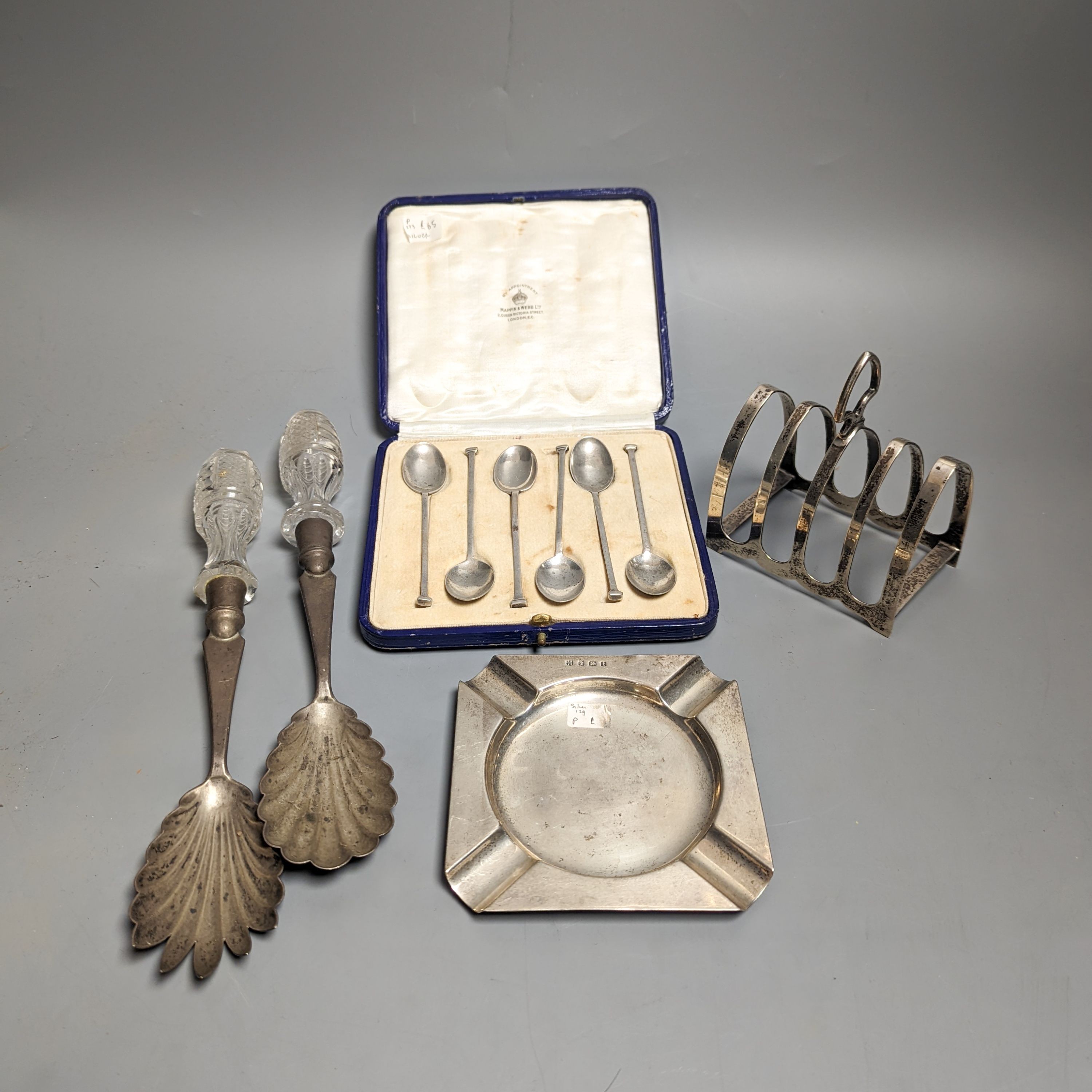 A pair of Edwardian glass handled silver salad servers, William Hutton & Sons, London, 1902, 26.8cm, a cased set of six silver teaspoons, a silver toastrack and a silver ashtray.
